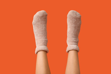 Legs of young woman in warm beige socks on orange background