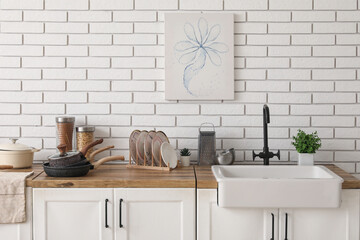 Different dishware and sink near white brick wall in kitchen
