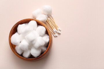 Wooden bowl with cotton balls and swabs on beige background
