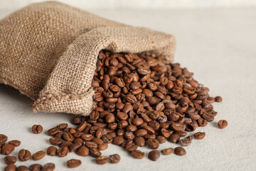 Burlap bag with aromatic coffee beans on light table, closeup