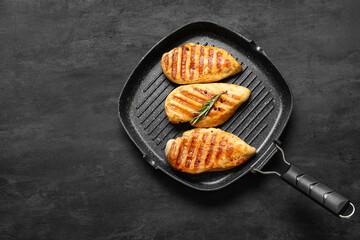 Frying pan with tasty grilled chicken breast, rosemary and peppercorns on black grunge background