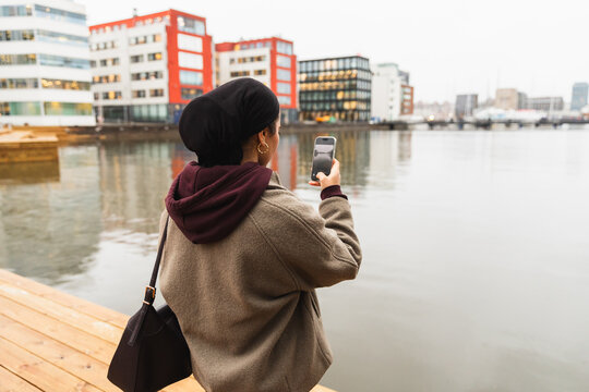 Student in niqab by city river enjoying coffee and photography