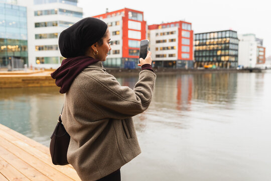Student in niqab by city river enjoying coffee and photography