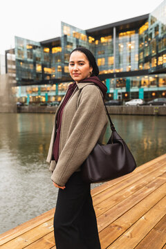 Woman in niqab posing by city canal with modern buildings