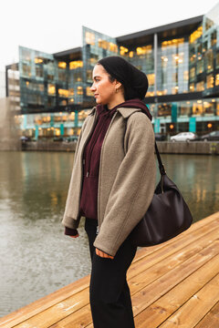 Woman in niqab posing by city canal with modern buildings
