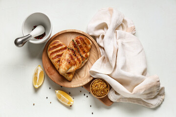 Wooden plate with tasty grilled chicken breast, thyme, Dijon mustard and lemon slices on white...