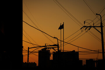 Silhouette of flags, buildings and wires against orange sunset sky