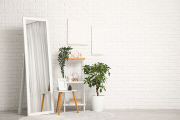 Shelving unit, floor mirror and houseplants near white brick wall in interior of room