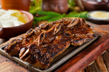 Short ribs, served on wood with blurred side dishes in the background. Assado de tira