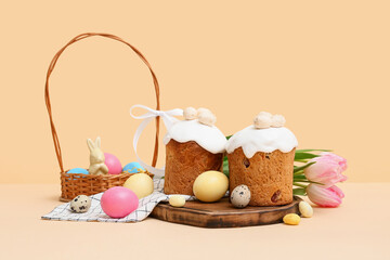 Wooden board with sweet Easter cakes, eggs and beautiful tulip flowers on yellow background