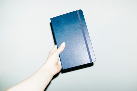 Hand holding dark blue paper notebook with hard direct flash