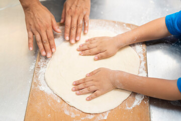 Parent and child flattening pizza dough together on wooden board