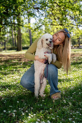 Beautiful young woman with her pet poodle playing on the grass in the park in the spring 