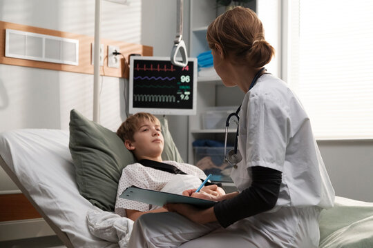 Female doctor visiting young patient in hospital bed taking notes