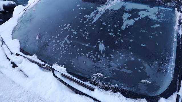 Snow-covered car windshield with frost patterns in winter