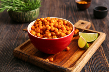 Bowl with tasty fried chickpeas, lime, rosemary and spices on wooden background