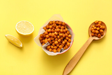 Bowl and wooden spoon of tasty fried chickpeas with lemon on yellow background