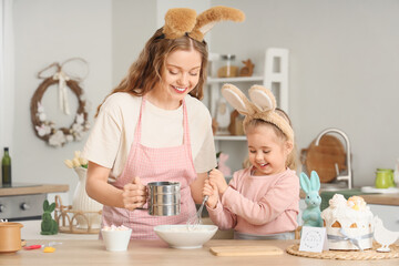 Happy mother and her cute daughter in bunny ears making dough for Easter cake at home