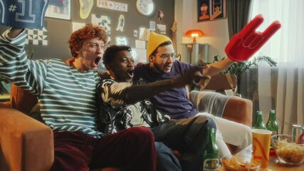 Three young multi-ethnic friends watching sports game on TV, yelling and clapping hands in excitement as celebrating victory on sofa with snacks and drinks nearby in living room. Zoom shot