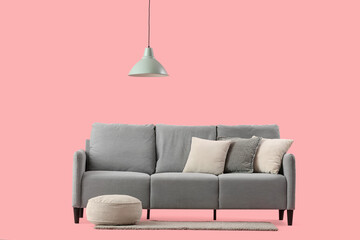 Stylish grey sofa with cozy cushions and pouf on pink background