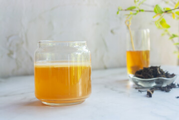 a jar of Jun tea fermented probiotic drink made from green tea and honey put on white table with raw honey and loose leaves green tea.