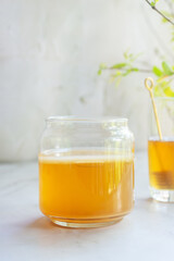 a jar of Jun tea fermented probiotic drink made from green tea and honey put on white table with raw honey and loose leaves green tea.