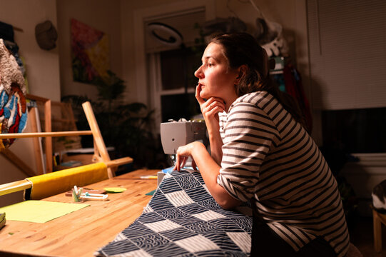 Woman Reflecting While Sewing at a Wooden Table