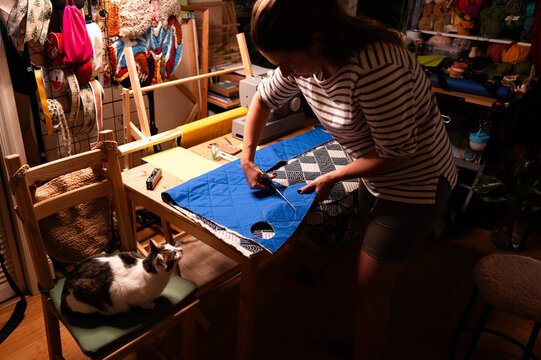 Woman Cutting Blue Quilted Fabric with Cat Nearby