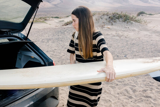 Surfer taking her surfboard out of a car at Famara beach, Lanzarote