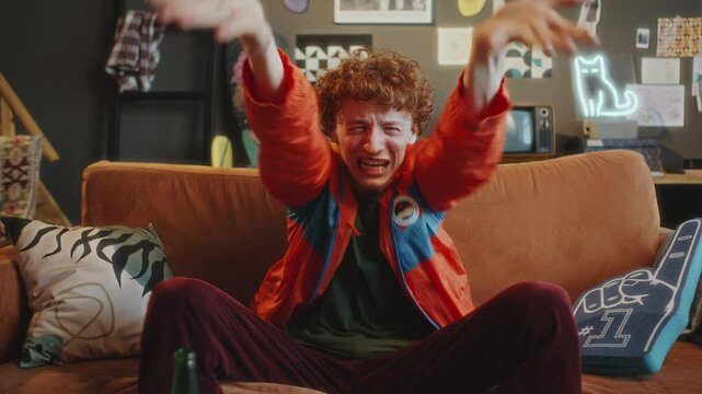 Upset sports fan sitting on couch in modern living room, watching game on TV, emotionally reacting to disappointing loss by his favorite team. Zoom shot