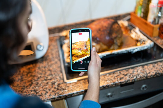Food blogger recording roasted pork with smartphone in kitchen