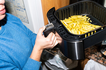 Woman cooking french fries using a modern domestic air fryer appliance