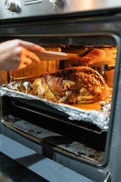 Chef basting pork shoulder in oven with wooden spoon