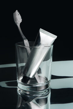 Toothbrush and a cream tube in a glass against a dark background