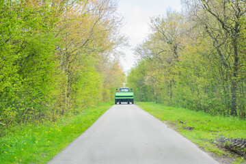 Green Farming Vehicle on Tree-Lined Road in Spring Landscape
