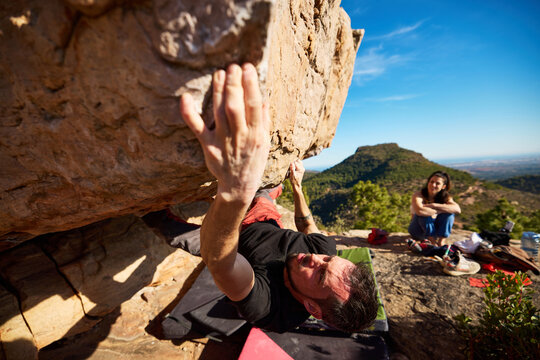 Man climbing on boulder with friend aside