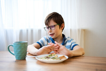 Stubborn boy with a displeased face refuses to eat on a plate, sits in the kitchen without appetite. Upset teenage boy does not want to eat tasteless food, loss of appetite.