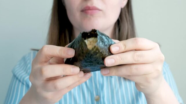 Young woman holding korean samgak with tuna close-up on grey background.
