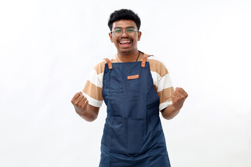 Fototapeta premium Excited asian coffee shop owner in blue apron celebrating, making fist pump and shouting for joy, achieve goal, standing against white background