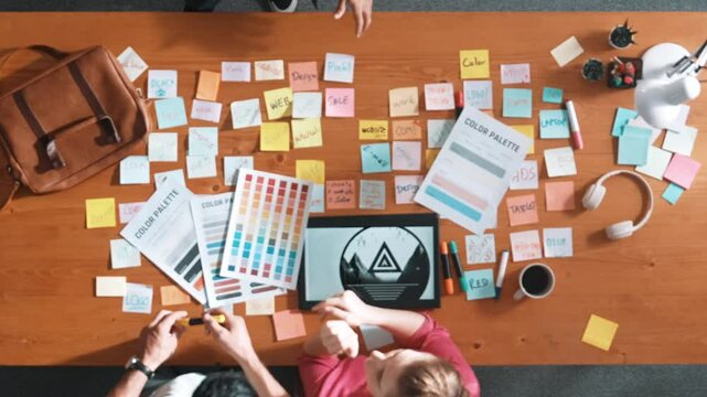 Top view of smart designer holding color palette while project manager looking at design and choosing color for program. Professional businesswoman taking a note while design creative logo. Symposium.