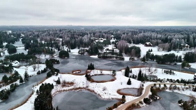 Aerial footage of partially frozen lakes or ponds with revealing of winter landscape of dark forest.