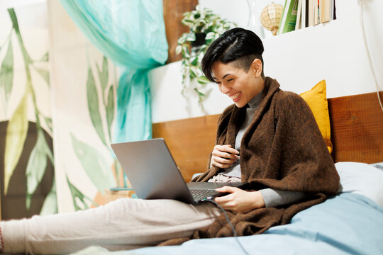 Cheerful woman in bedroom using laptop computer