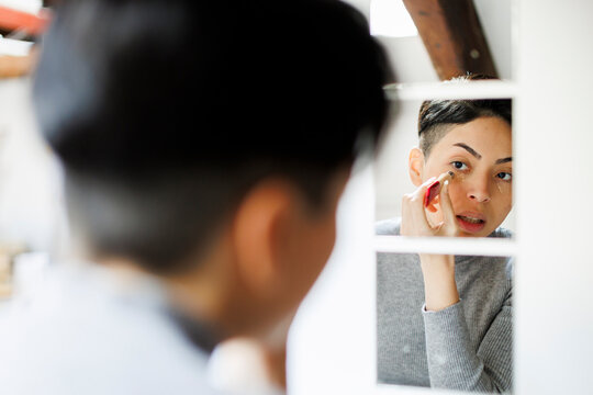 Woman's mirror reflection in apartment bathroom doing her makeup