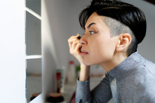 Woman in apartment bathroom applying eye liner in front of mirror