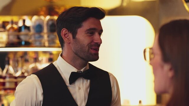 Closeup good looking smiling smart bartender friendly conversation talking VIP customer at beverage counter luxury making great first impression professional barman costume greeting guess. Vinosity.