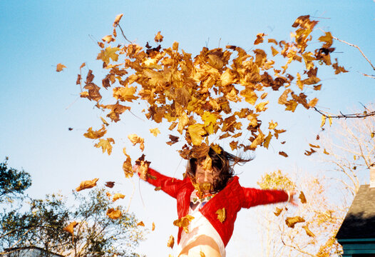 Child happily throws leaves into the air while playing outside in fall