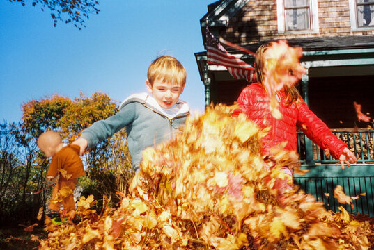 Candid film moment of siblings playing in pile of leaves
