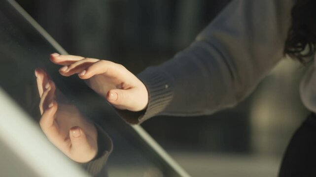 Woman is touching a glass window with her hand. The reflection of her hand is visible in the window