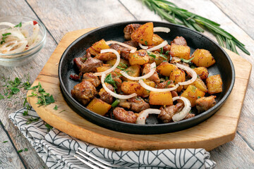 Fried potatoes with meat and onions in a frying pan. Served on a wooden board on the table