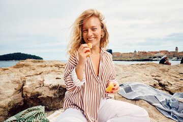 Happy woman eats an orange on the beach